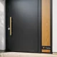 Puerta de entrada negra mate con tirador dorado y panel de roble; acabados en tendencia en España: Que acabados de puertas de entrada estan en tendencia en Espana